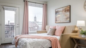 Et soveværelse med en seng, en sofa, et vindue med gardiner, et billede på væggen og en lampe på et sengebord.