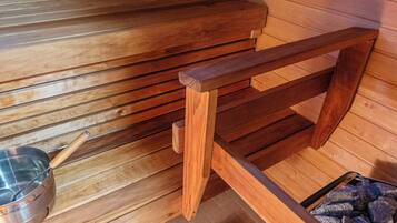 Una sauna con panche in legno, una bacinella metallica e un contenitore riempito di pietre.