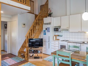 Een moderne keuken met witte kastjes, een magnetron, een fornuis en een vaatwasser. Een houten trap leidt naar een verdieping erboven.