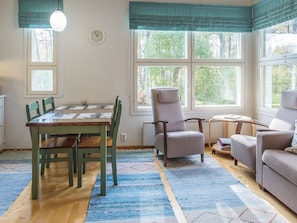 A room with a dining table, chairs, a sofa, a chair, a small table with a lamp, and a clock on the wall.