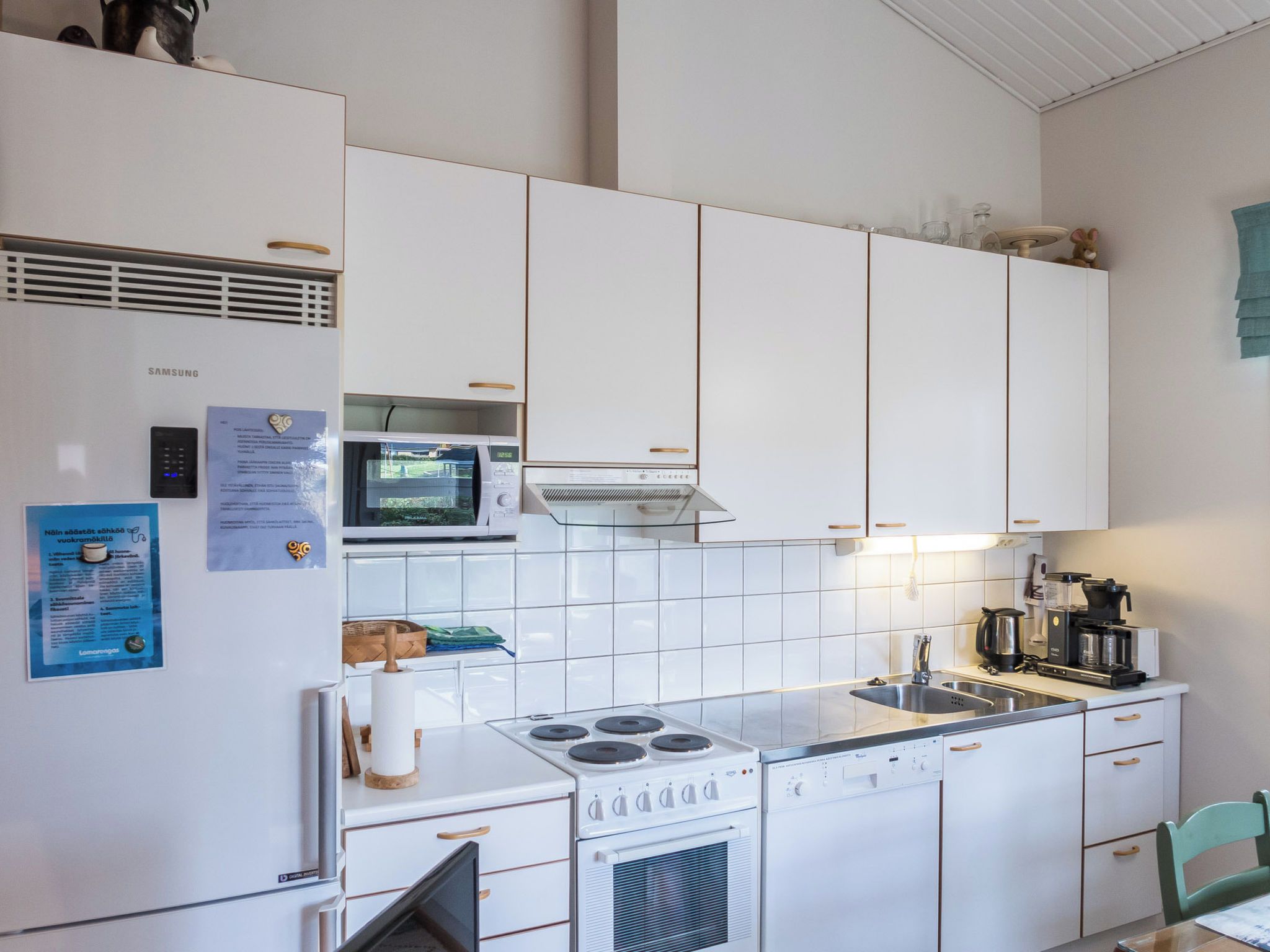 Kompakti keittiö, jossa on valkoiset kaapit, mikroaaltouuni, liesi ja kahvinkeitin.