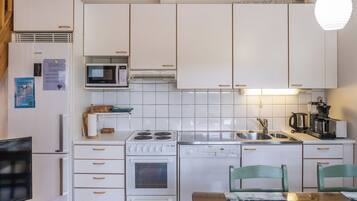Et moderne køkken med hvide skabe, mikroovn, komfur og opvaskemaskine. Der er et spisebord med stole og en hængende lampeskærm.