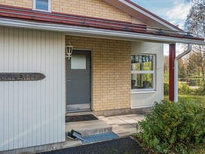 Een gebouw met een grijze deur, een bord waarop 'OPIKATTI' staat en een klein portaaltje met een bankje.