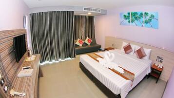 Habitación de hotel con cama, escritorio, silla, televisión, ventana con cortinas y un cuadro en la pared.