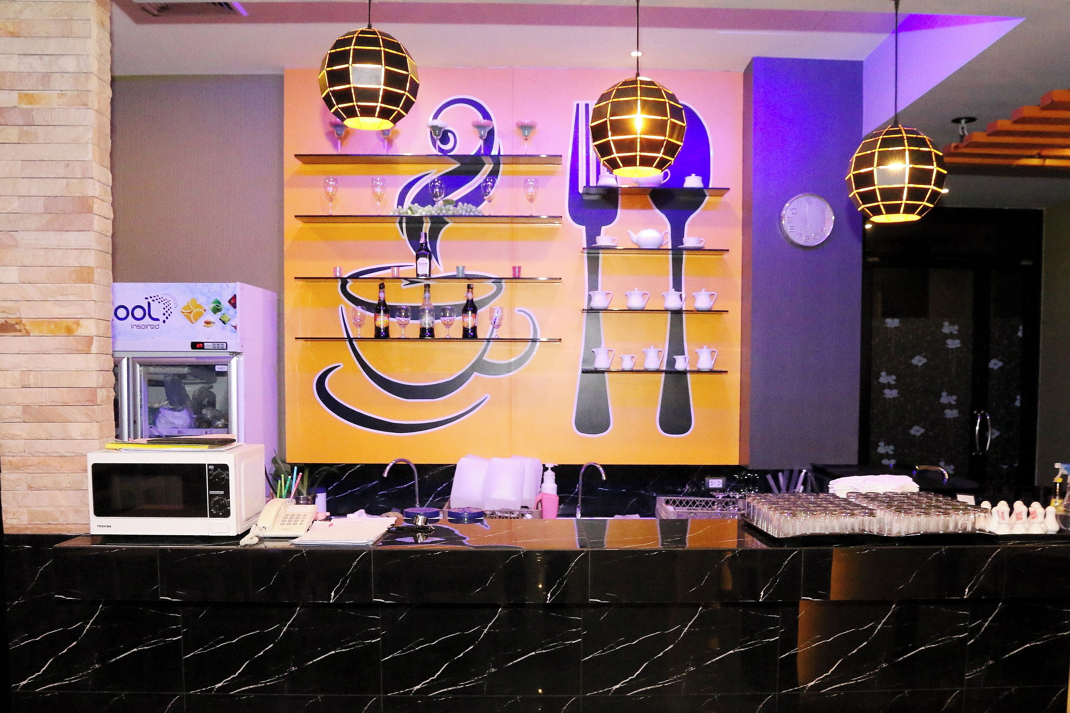 A hotel reception area with a modern design, featuring a reception desk, a microwave, and a decorative wall with shelves displaying items.