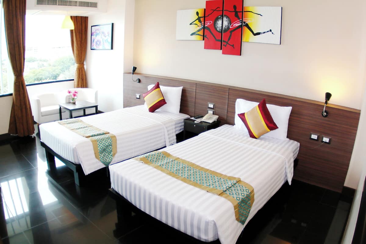 A hotel room with two beds, a desk, a chair, and artwork on the wall.