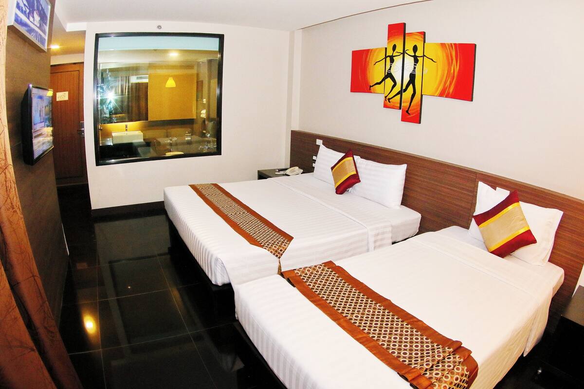 A hotel room with two beds, a large window, a painting on the wall, and a TV on the left.
