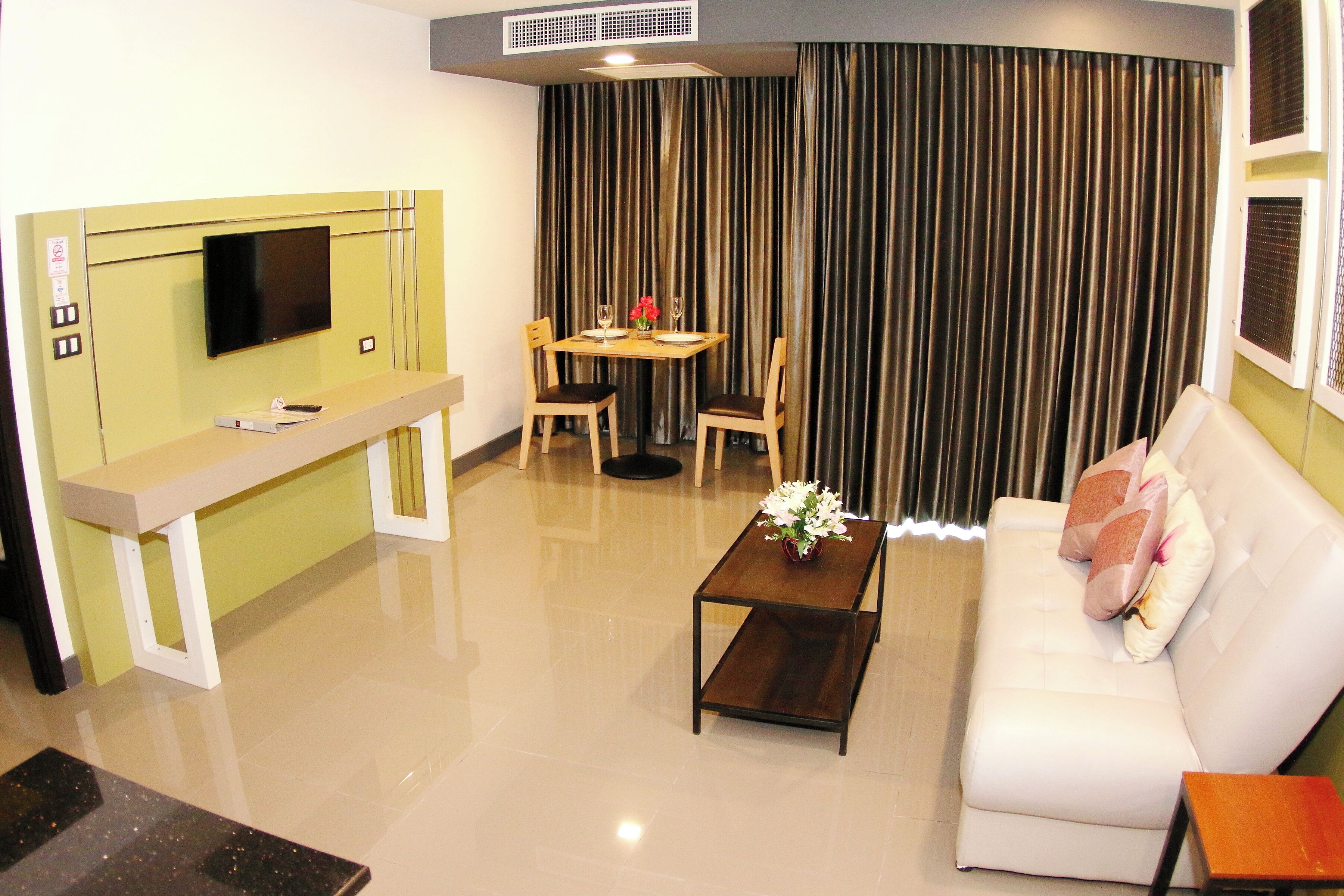 A modern living room with a sofa, a coffee table, a dining table with chairs, a TV mounted on a cabinet, and a large curtain.