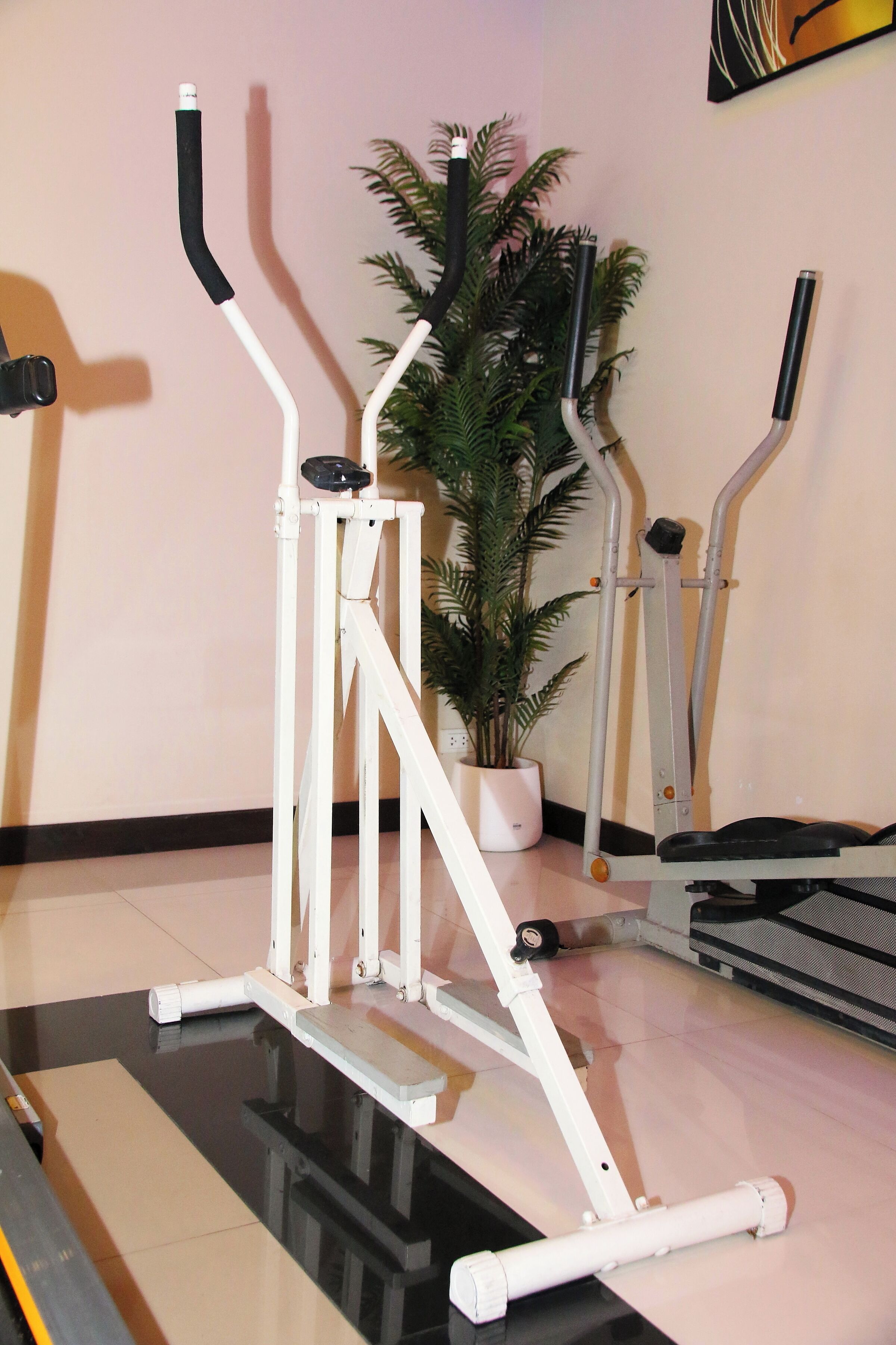Una máquina de ejercicio con un panel de control, una cinta de correr y una planta en maceta al fondo.