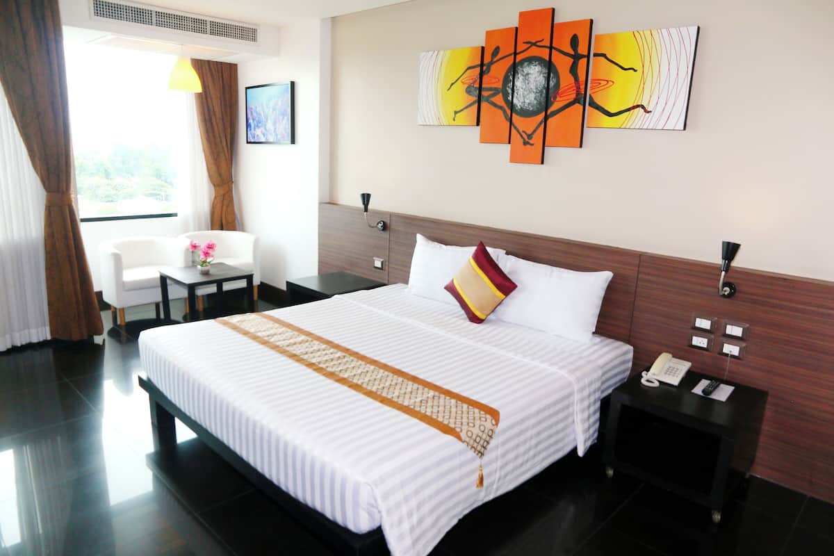 A hotel room with a large bed, a bedside table with a phone, a nightstand, a chair, and a window with curtains.