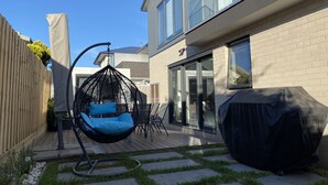 Moderni talo, jossa on riipputuoli, katettu grilli ja patio, jossa on puinen terassi ja nurmikko.