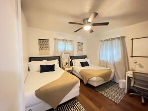 Two single beds with matching headboards and footboards, a desk, and a ceiling fan are featured in this hotel room.