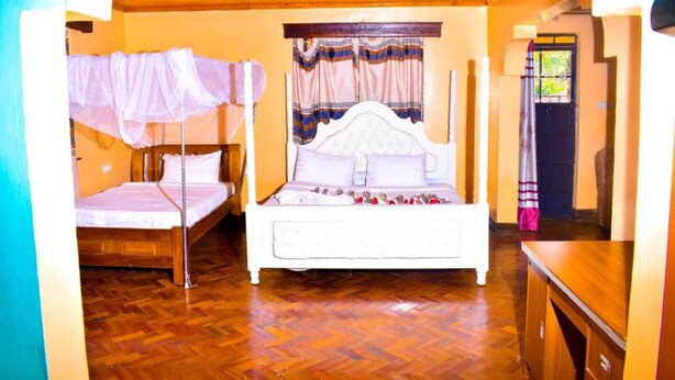 Een slaapkamer met een houten vloer, een bed met een wit hoofdeinde en een raam met gordijnen.