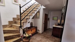 A staircase with marble steps leading to a landing, a wooden dresser with a vase of flowers, and a desk with a lamp.