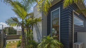 Een modern huis met een donkere gevel, grote ramen en een kleine tuin met palmboompjes en een rotsenbed.