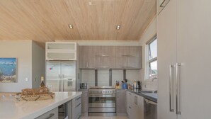 Een moderne keuken met roestvrijstalen apparatuur, een groot eiland en een houten plafond.