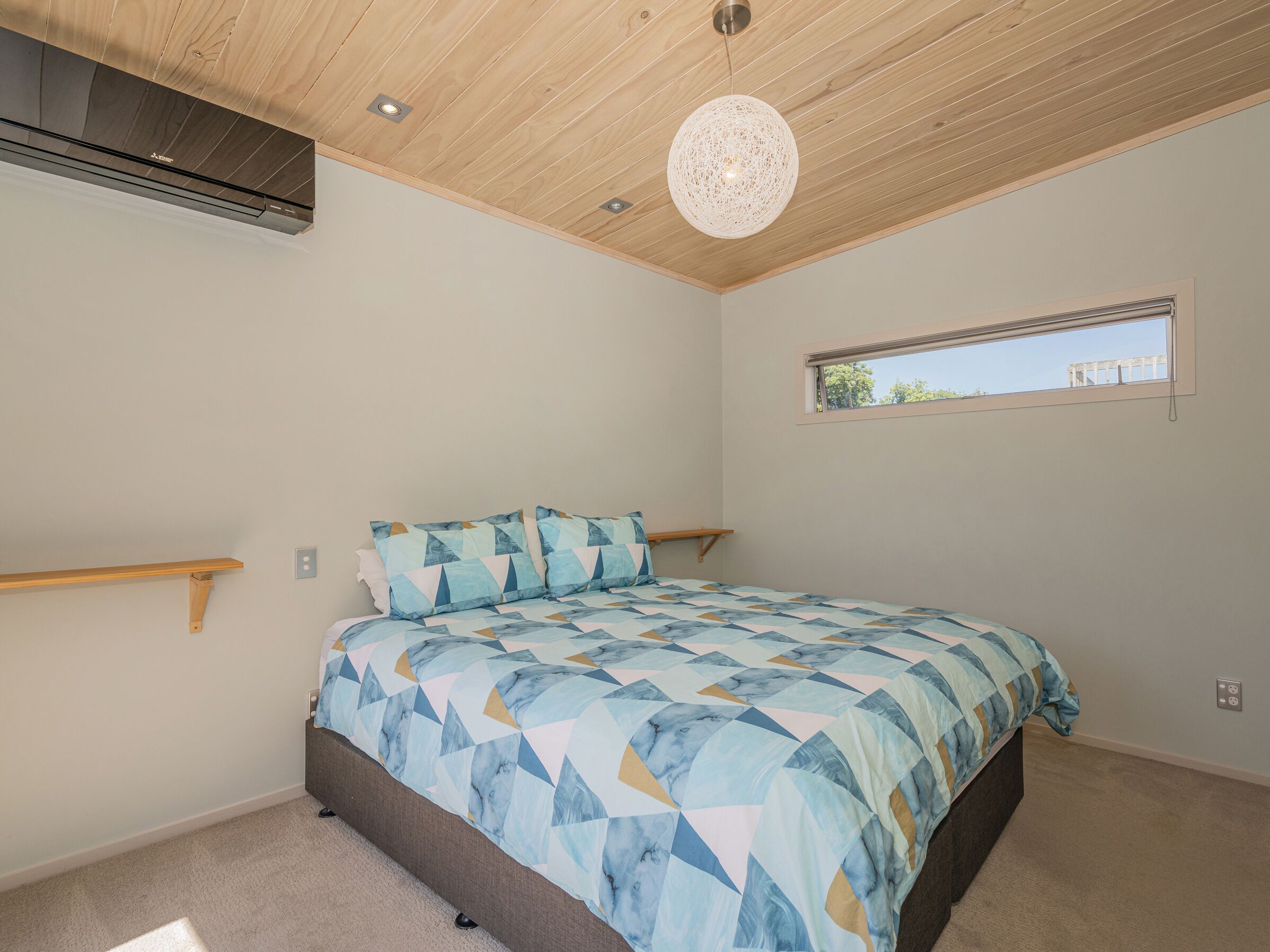 Une chambre à coucher avec un lit, un plafond en bois, une fenêtre et un luminaire suspendu.