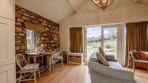 Una habitación acogedora con pared de piedra, suelo de madera, una mesa de comedor con sillas, un sofá y un ventanal con cortinas.