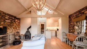 Una sala de estar acogedora con chimenea, un sofá y una televisión. Hay una zona de cocina con pared de piedra y una mesa de comedor con sillas.