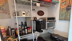 Una cocina compacta con cafetera, tostadora y una estantería con diversos alimentos.