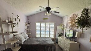 Un dormitorio con cama, cómoda, televisor y ventilador de techo.