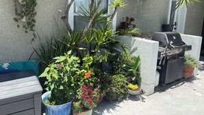 Un patio con una parrilla, plantas en macetas y un banco azul para guardado.