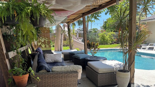 Un espacio de descanso al aire libre con mobiliario de mimbre y plantas en macetas, con vistas a una piscina.