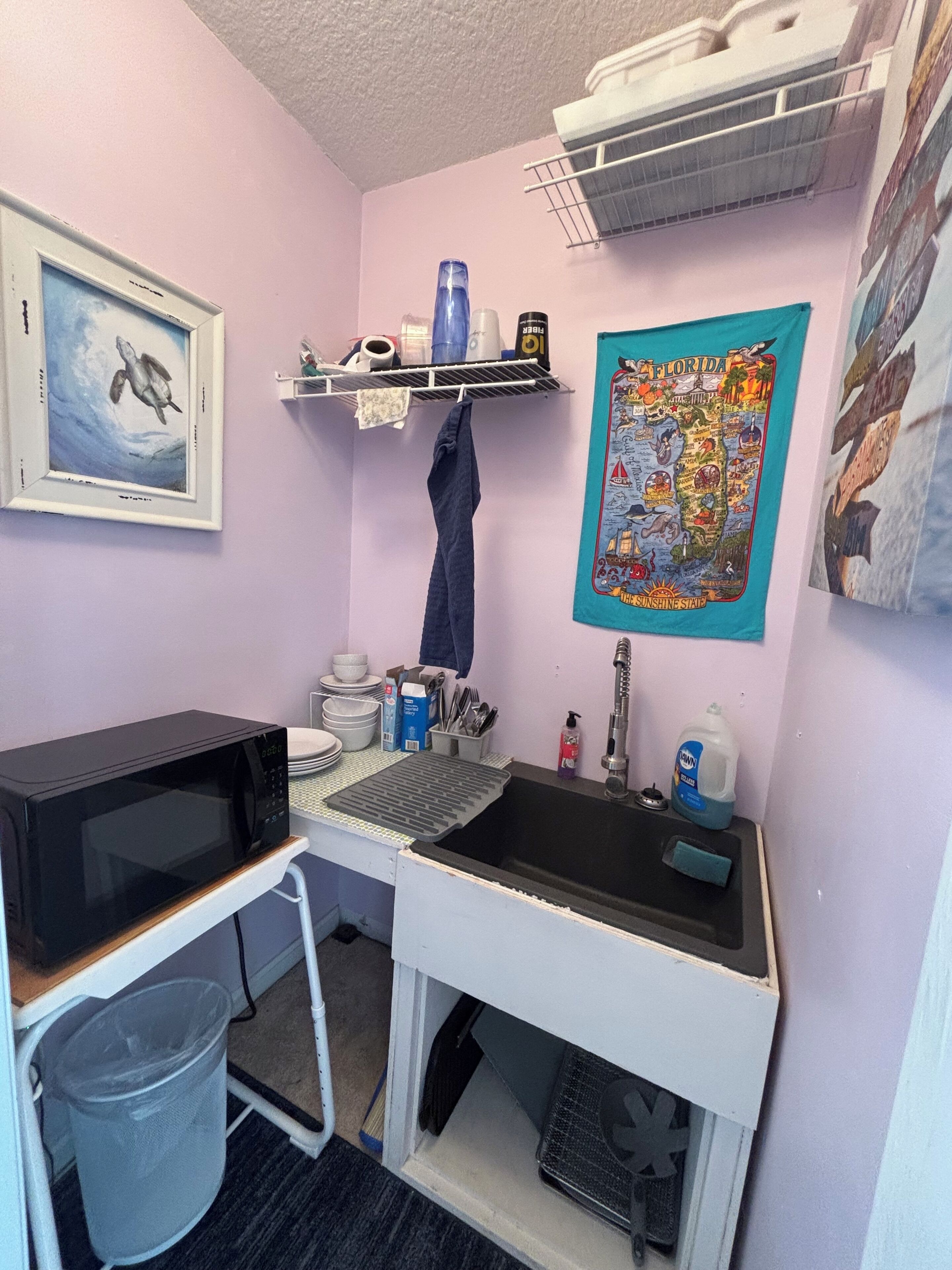 A compact kitchenette with a microwave, sink, and storage shelves.
