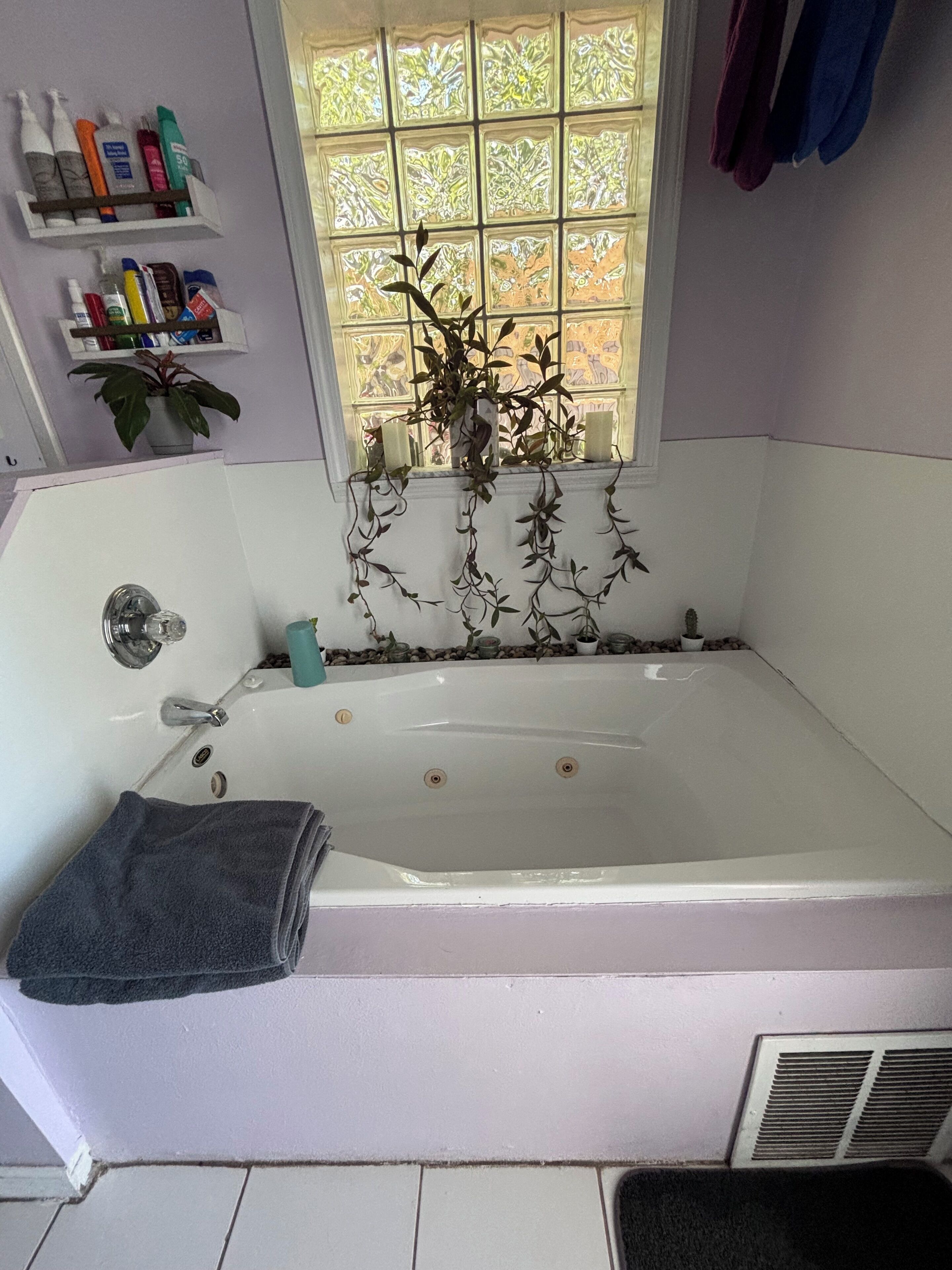A bathroom with a bathtub, a window with decorative glass, and a shelf with toiletries.