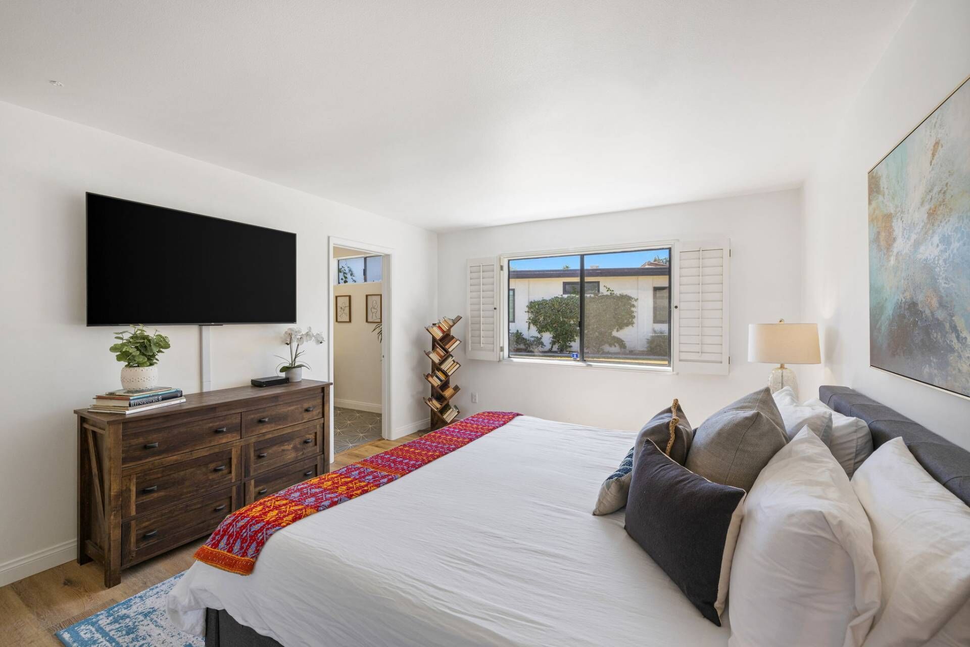 A bedroom with a bed, a TV, a dresser, a window, and a painting.