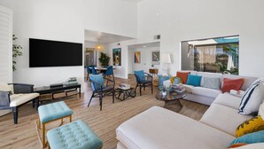 A spacious living room with a sofa, ottomans, a coffee table, and a dining area with chairs and a table. - Modern Chic Condo at Rancho Las Palmas (Rancho Mirage)