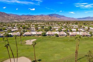 A golf course with a residential area in the background, featuring houses and palm trees.