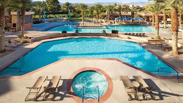 Un área de piscina con varias piscinas, sillas de descanso y palmeras.