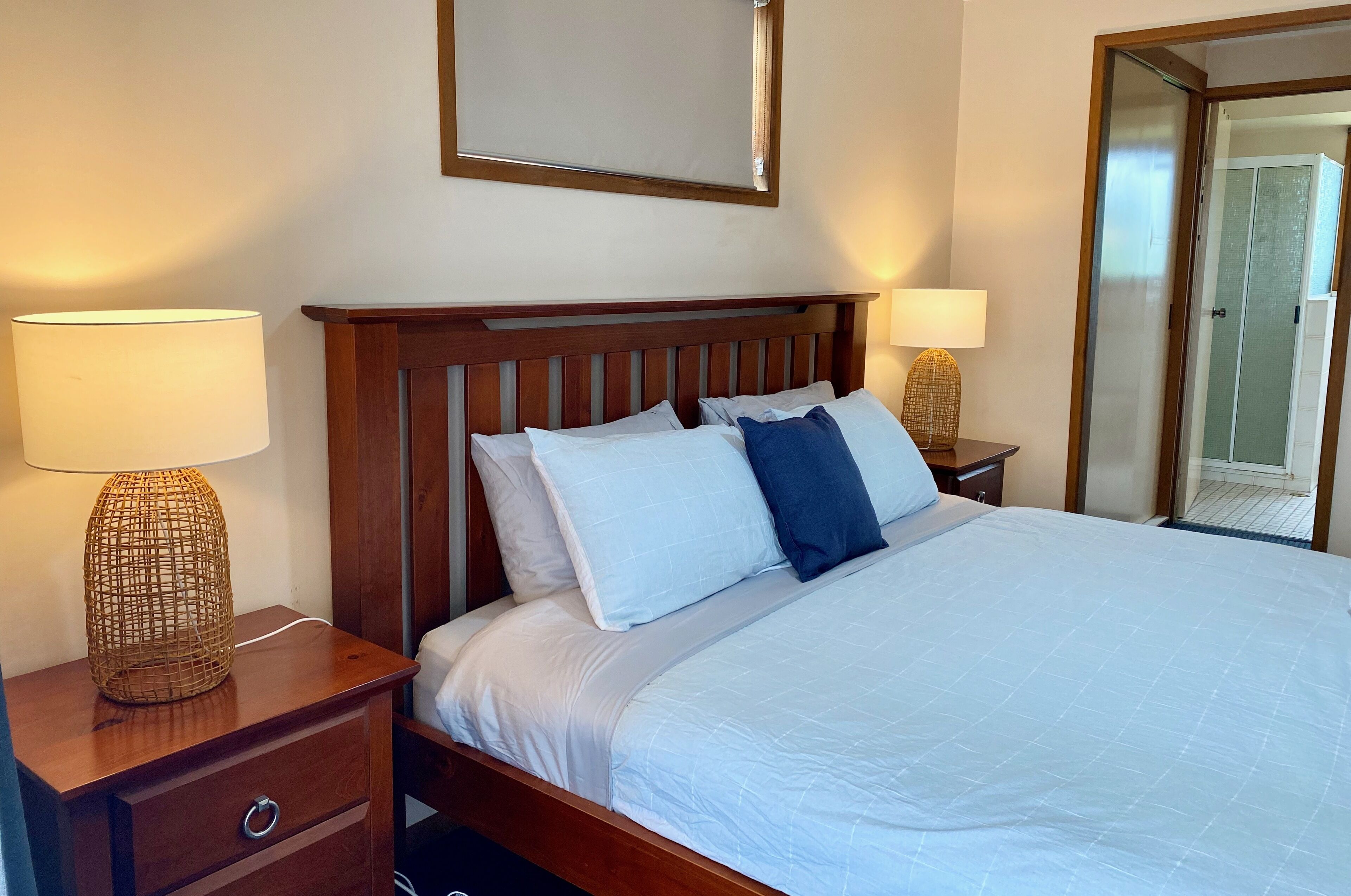 A neatly made bed with white and blue pillows, wooden headboard, and bedside lamps on wooden nightstands.
