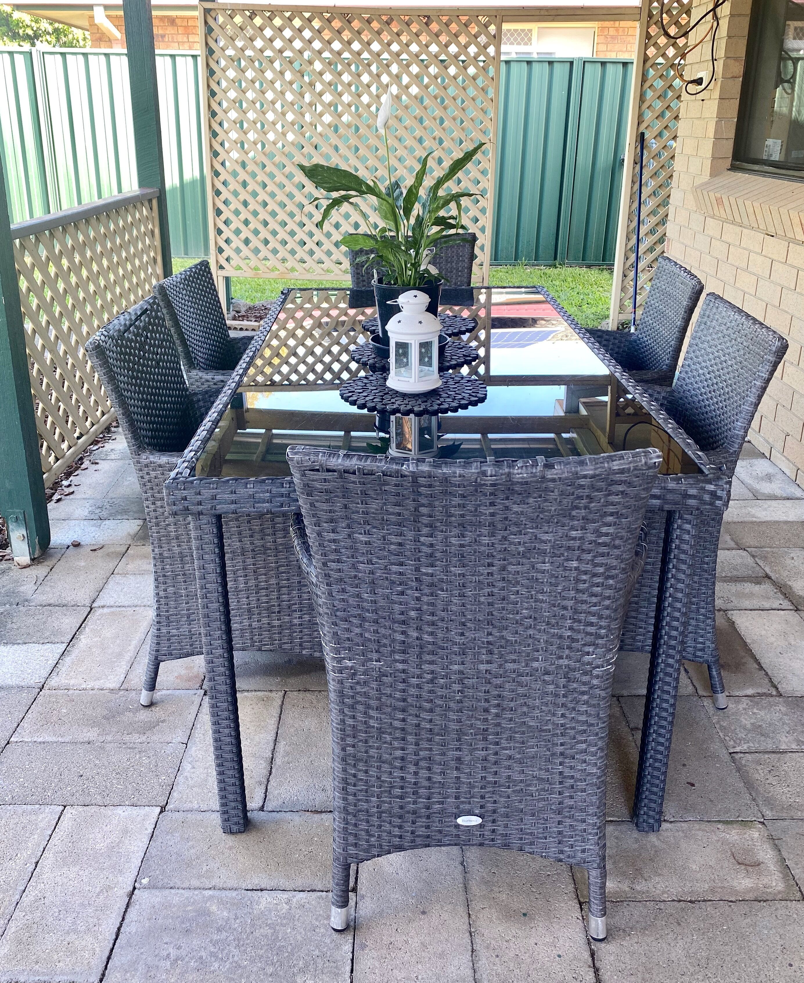 A patio with a glass-top table surrounded by wicker chairs, a potted plant, and a white lantern.