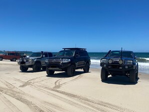 Three off-road vehicles parked on a sandy beach with the ocean in the background.