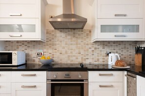 A modern kitchen with white cabinets, a stainless steel range hood, a microwave, an oven, a bowl of lemons, and a loaf of bread on the counter.