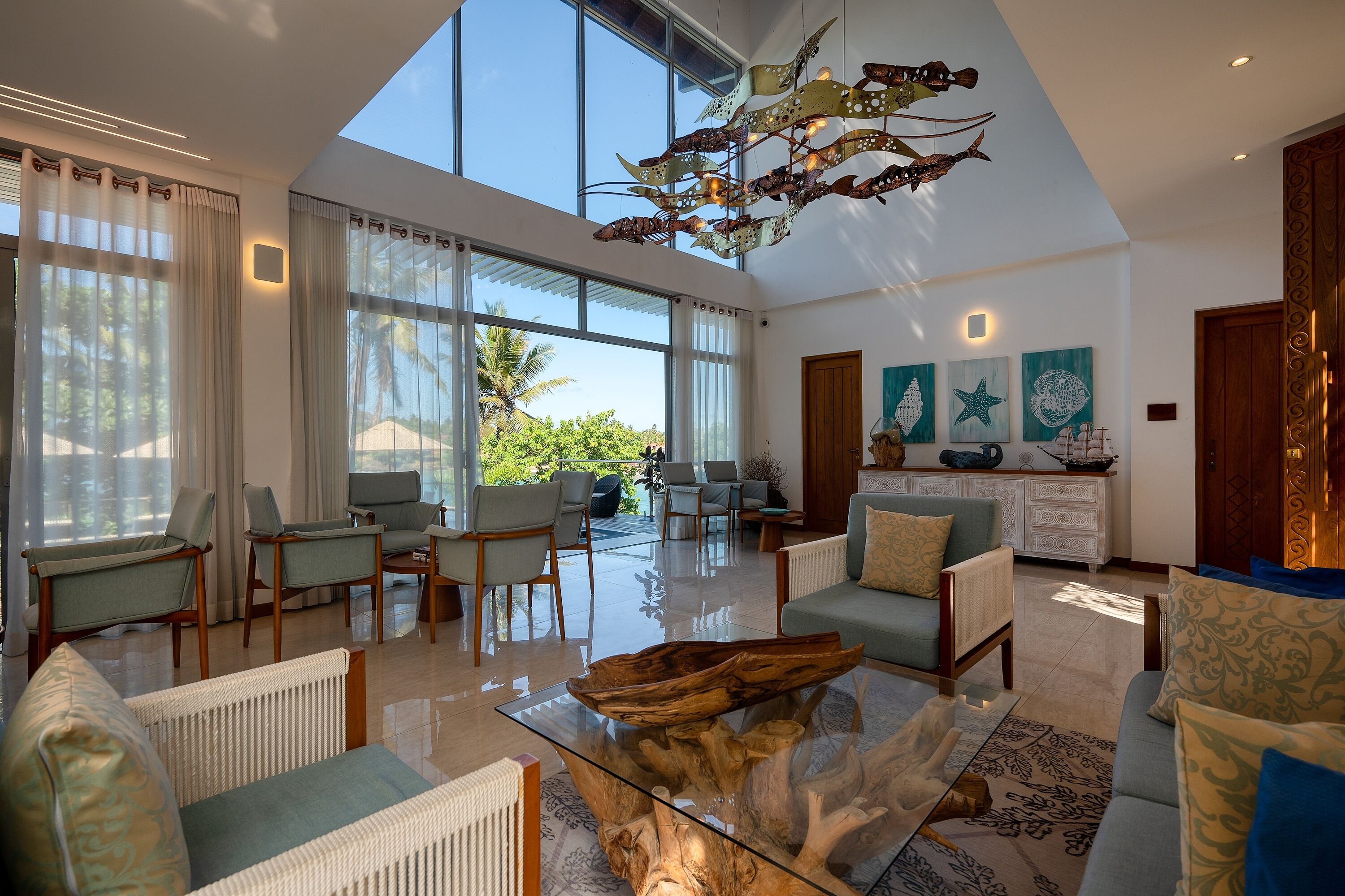A spacious living room with a glass coffee table, comfortable seating, large windows, and a modern chandelier.