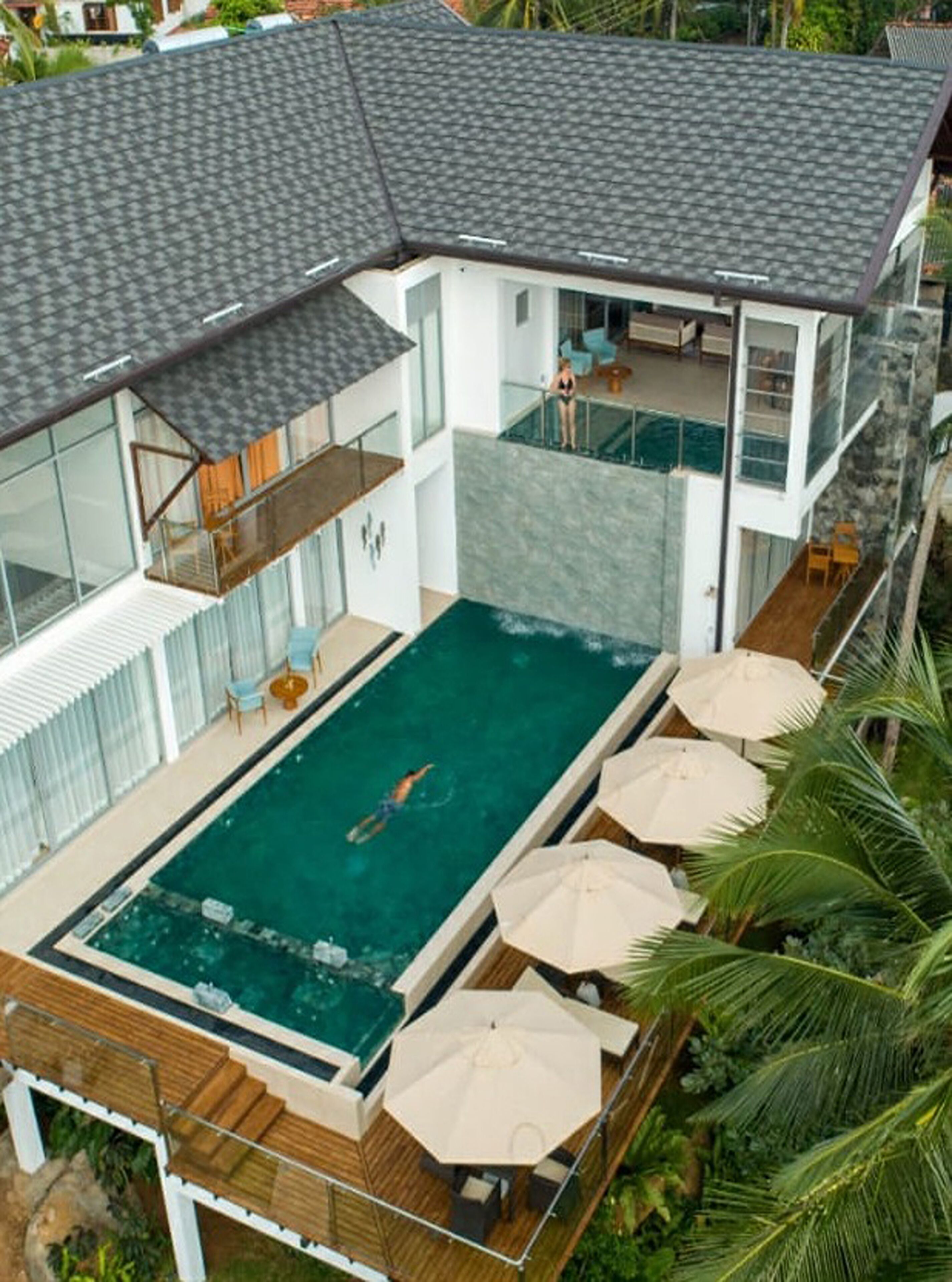 Een modern huis met een groot zwembad, een houten terras en zitplaatsen buiten.