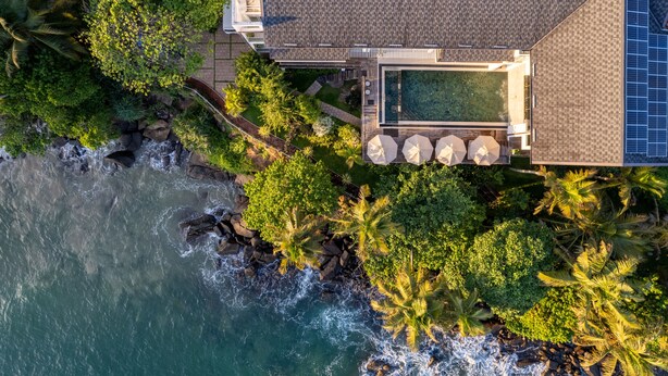 An aerial view of a coastal property with a swimming pool, solar panels, and lush greenery.