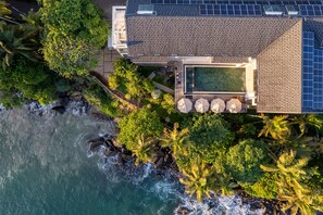 An aerial view of a coastal property with a swimming pool, solar panels, and lush greenery.
