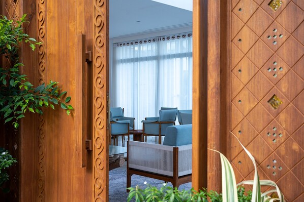 A wooden door with intricate carvings leading to a room with a large window, a sofa, and a table.