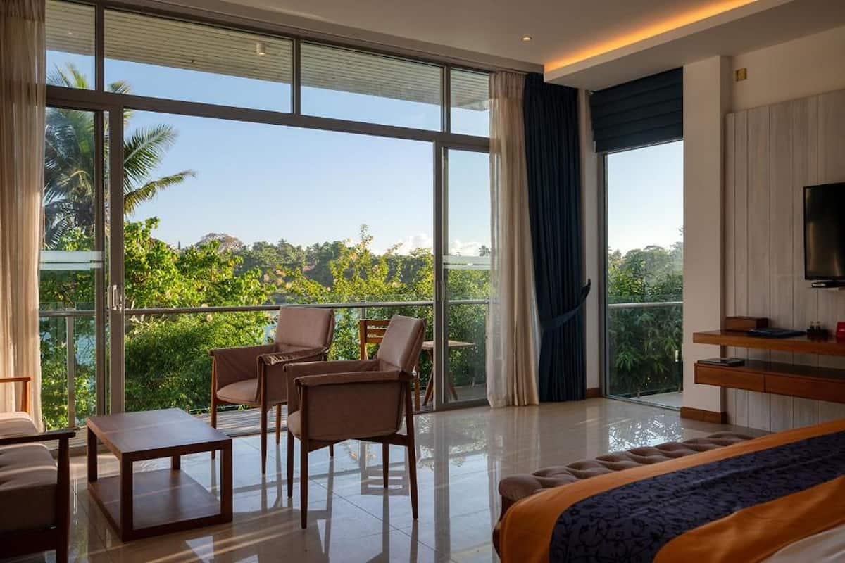 Une pièce spacieuse dotée d’une grande fenêtre, d’un lit, d’une télévision et d’un balcon avec des chaises.