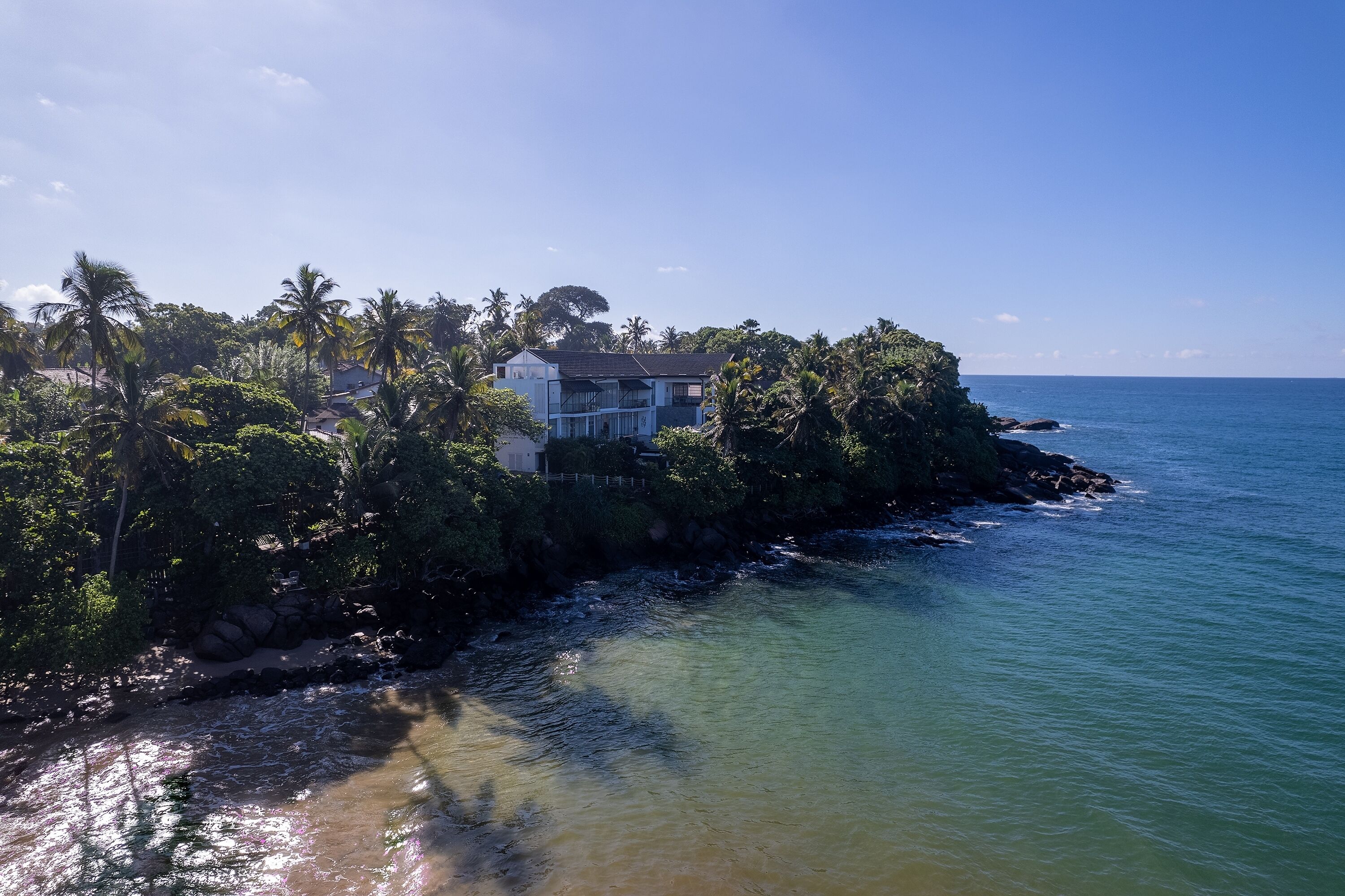 A coastal property with a house surrounded by dense tropical vegetation and a clear view of the ocean.