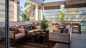 A spacious outdoor seating area with a sofa, chairs, and wooden stools, overlooking palm trees.