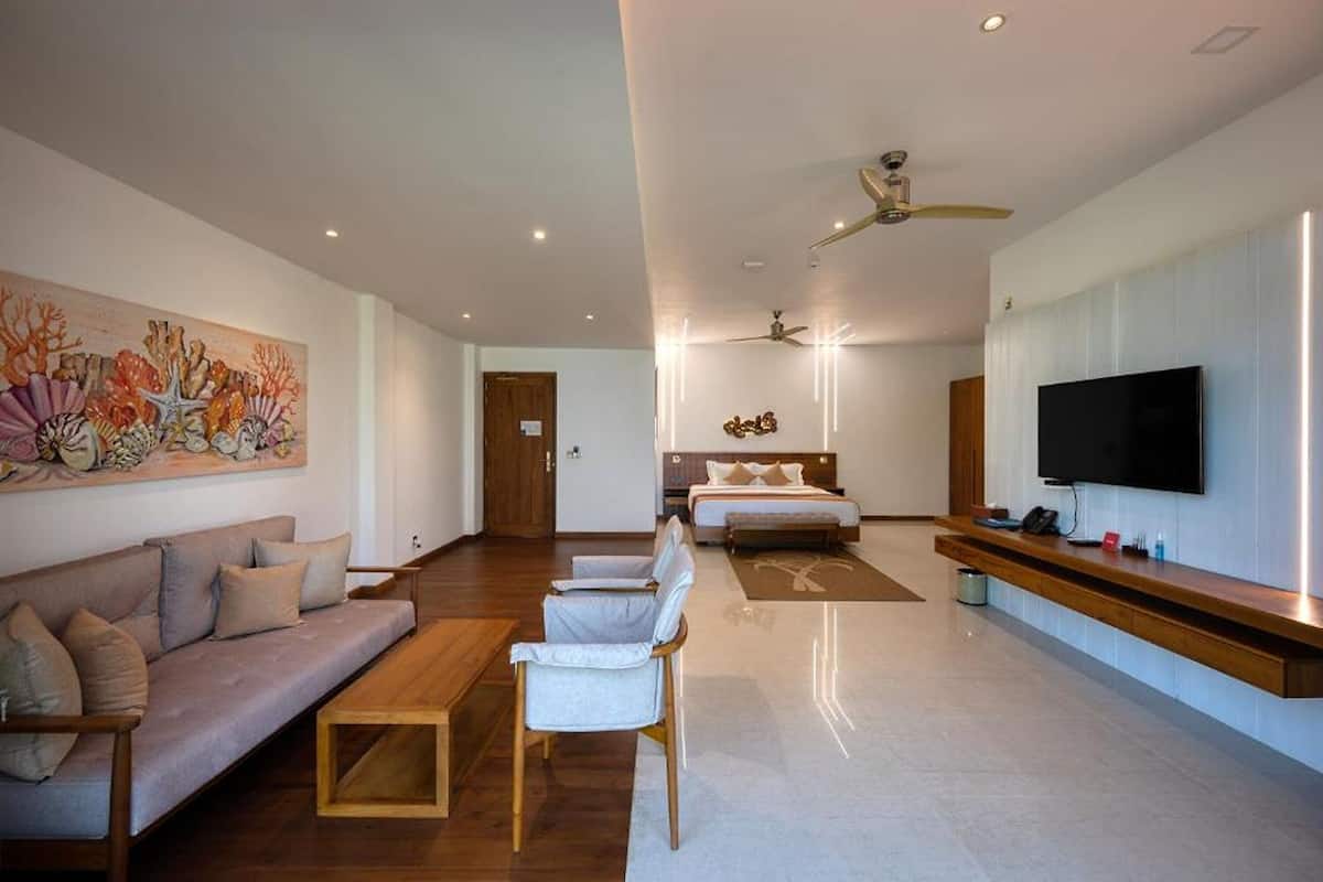 Une chambre d’hôtel moderne équipée d’un canapé, de fauteuils, d’un lit, d’une télévision et d’un ventilateur de plafond.