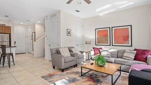 A modern living room with a grey sofa, a coffee table, and a colorful rug. There is a staircase leading to another room, and a kitchen area is visible in the background. - ♥︎ Disney-3 miles ♥︎ Private HotTub ♥︎Top Resort♥︎ (Kissimmee)