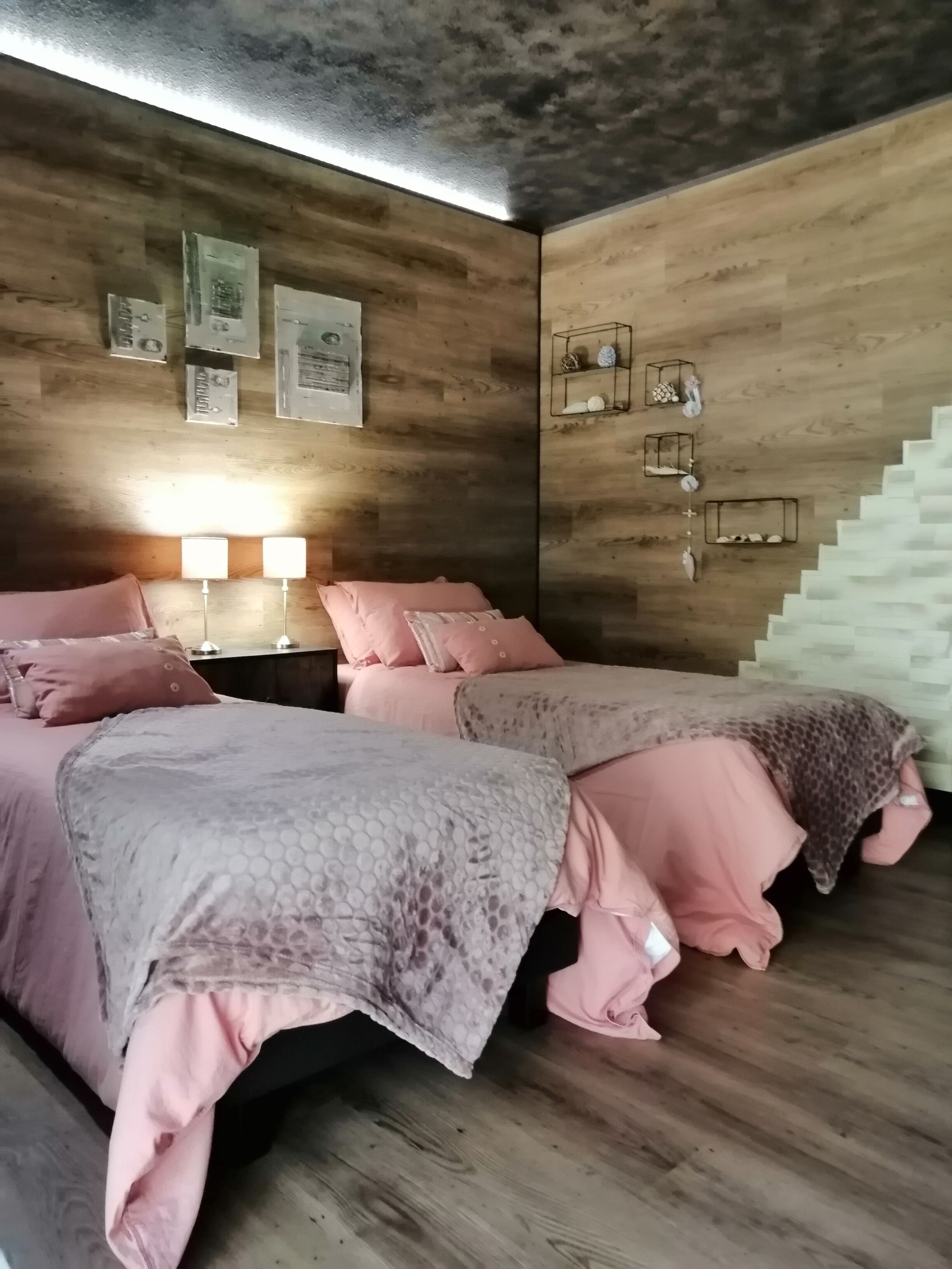 A bedroom with two beds, wooden walls, and a staircase.