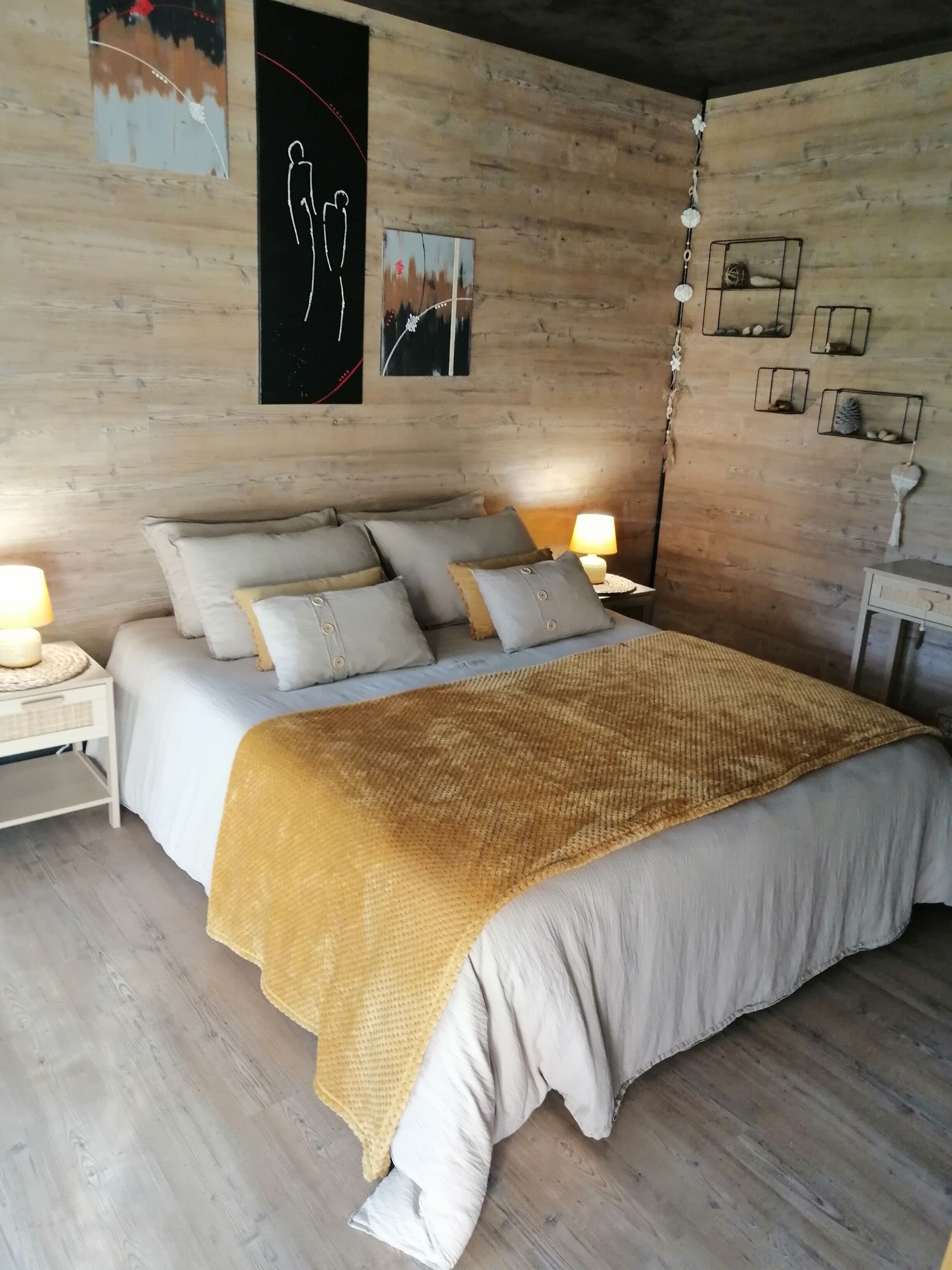 A bedroom with a large bed, multiple pillows, a bedside table with a lamp, and wall art.