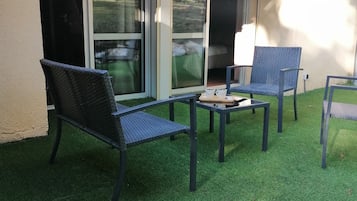 Un patio al aire libre con césped artificial, dos sillas de mimbre, una mesita y una guirnalda de luces.